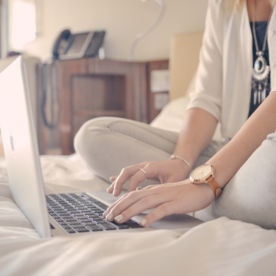 Mujer escribiendo en el ordenador sobre la cama